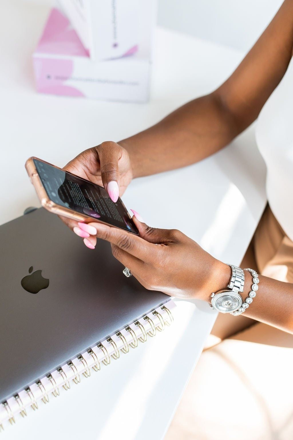 Person using a smartphone with an Apple laptop and notebook in the background