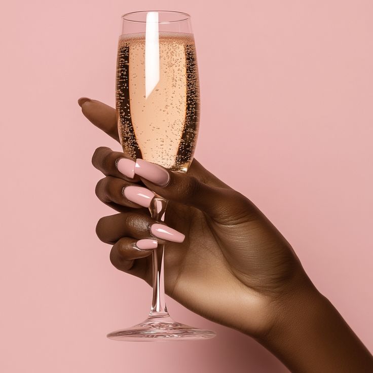 Hand holding a glass of sparkling wine against a pink background